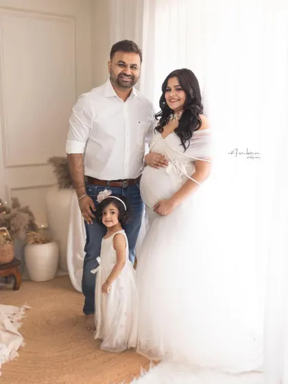 A classic family portrait taken during a maternity session. The family stands together in a light-filled studio, creating a clean, elegant image that focuses on their connection.