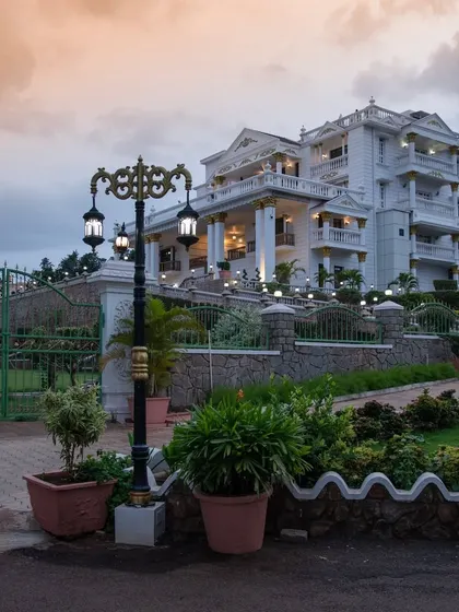 Another view of 'The Palace Promised' at twilight. The landscape design includes tiered gardens and stone retaining walls that navigate the natural slope of the land, adding to the estate's grandeur.