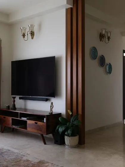 In the 'Earthy Chic' living room, we used vertical wooden rafters beside the television console. This design element cleverly conceals structural components while adding natural charm and visually expanding the space.