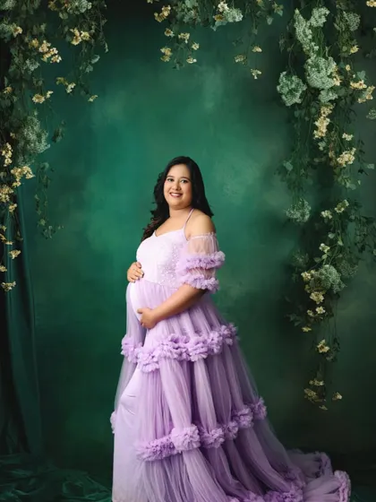 The combination of the lavender gown and the deep green floral backdrop creates a rich, enchanting atmosphere.