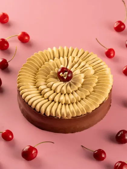 A top-down view of a beautifully piped black forest cake, surrounded by fresh cherries. This is an elegant product shot for a patisserie.