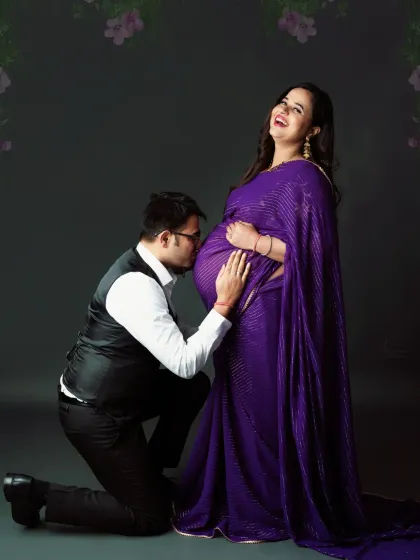 A joyful and candid moment. The dad-to-be kisses his wife's baby bump, bringing a smile to her face in this lovely purple saree shoot.