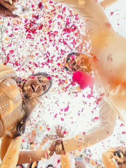 A unique low-angle shot of the couple during their Haldi, capturing their joyful expressions as they are showered with flower petals from above.