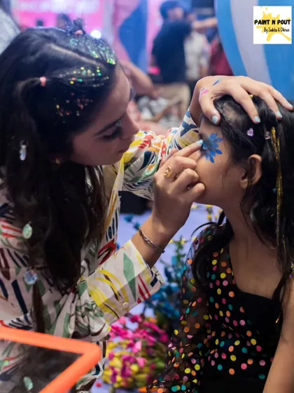 One of our artists in action, painting a blue flower on a young girl's cheek while her hair sparkles with our festival glitter.
