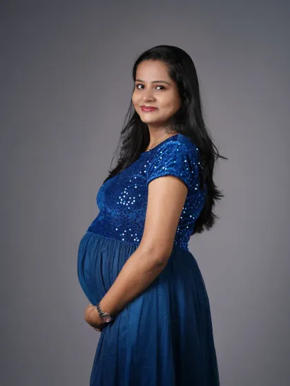 A simple and elegant studio portrait of an expecting mother in a royal blue sequined gown. The side profile and soft smile create a gentle and happy mood.