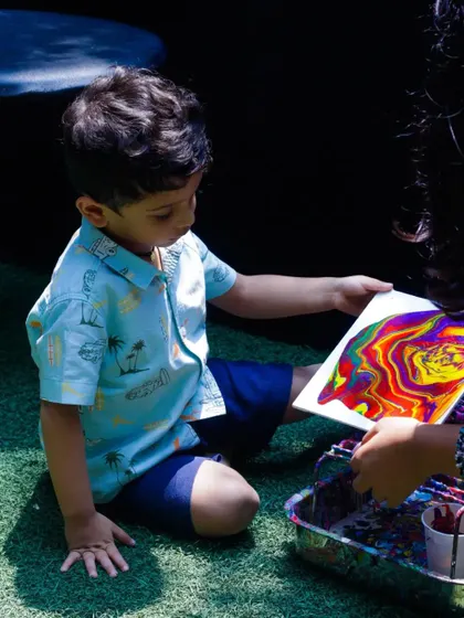 A young boy proudly looks at his colorful acrylic pour creation during our Father's Day event. We love seeing the pride and joy on kids' faces when they complete their art.
