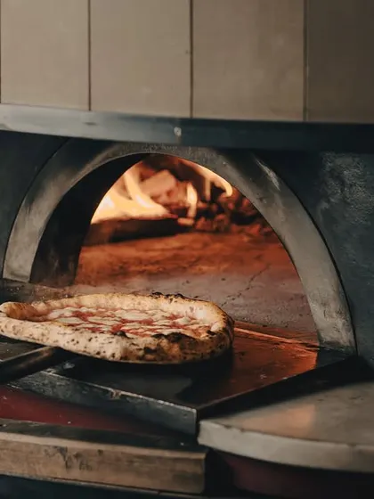 A pizza going into our custom-built wood-fired oven. The fire gives our pies their signature smoky char and flavour.