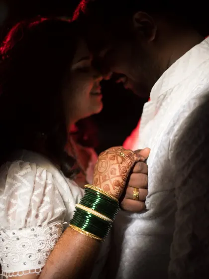 An intimate close-up shot focusing on the bride's hand on the groom's chest. The image highlights her henna and green bangles, telling a story of love and tradition.