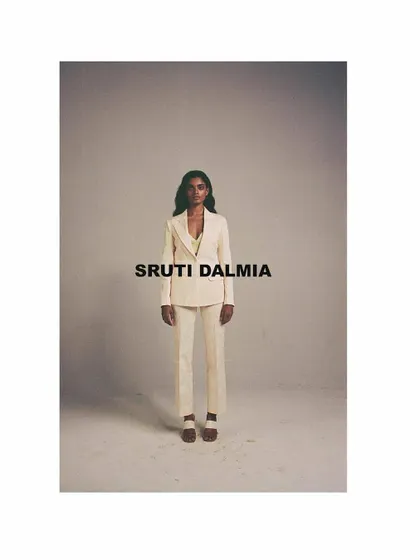 A minimalist look from the Sruti Dalmia campaign, featuring a clean, tailored off-white suit. The studio styling is stark and direct, focusing entirely on the garment's sharp silhouette and modern aesthetic.