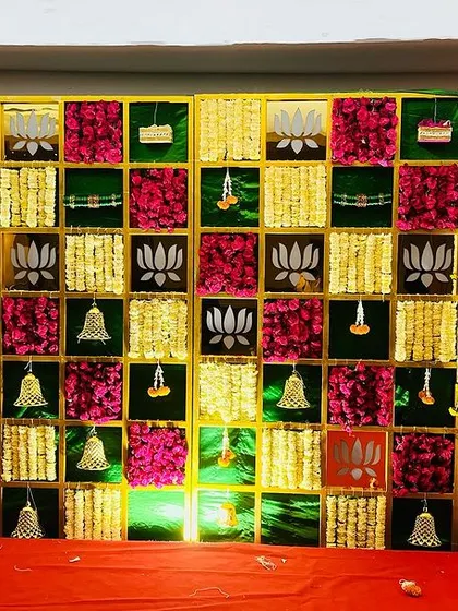 A vibrant and colorful backdrop for a baby shower, using panels of magenta, yellow, and green fabric. The design is accented with hanging bells and lotus motifs for a festive look.