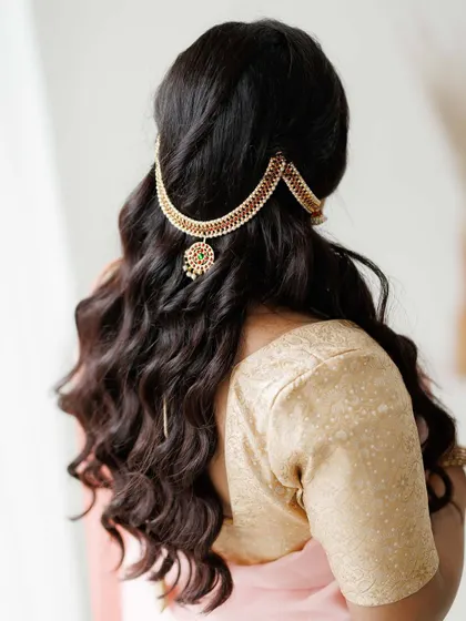 Hairstyling is just as important as makeup. This image details a traditional South Indian hairstyle with soft, open curls, elegantly accessorized with a statement hairpiece. This style is perfect for adding a touch of royalty to a saree look for any special occasion.