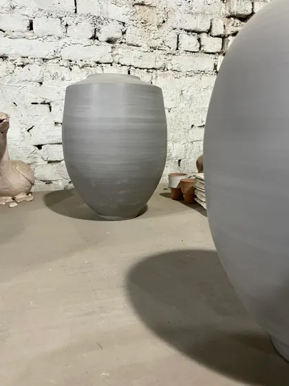 A tall, elegant vase waiting for its turn in the kiln. The clean lines and smooth surface show the precision of wheel-throwing, a quiet moment before the color and texture of the glaze are added.