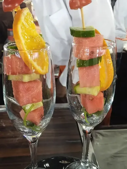 Watermelon and cucumber skewers garnished with orange slices, served in wine glasses for a refreshing and stylish treat.