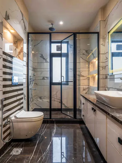 In this bathroom, I combined striped wall tiles with a marble-patterned wall for a dynamic effect. The black-framed shower enclosure and dark flooring ground the space and add a modern edge.