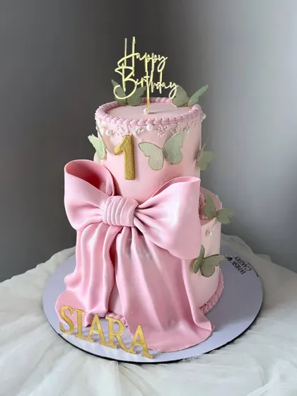 The big bow cake. This image shows how we customize designs, recreating a previous white cake in pink and adding sage green butterflies to match the birthday girl's dress.