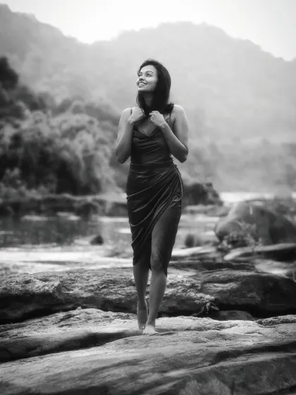 A beautiful black and white portrait of a woman walking barefoot on a rocky shore, with mountains in the background. Her joyful expression and the natural landscape create a feeling of peace and liberation.