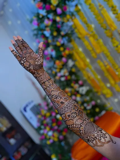A single arm view of a bridal henna design, set against a festive wedding backdrop.