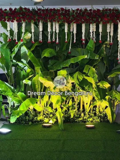 A close-up of the banana leaf backdrop, showing the beautiful contrast between the vibrant green leaves and the delicate white and red flowers. The uplighting adds a dramatic effect.