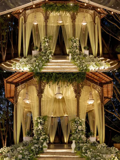This enchanting mandap design features soft, flowing drapes and pillars wrapped in white florals, illuminated by elegant chandeliers. The result is a dreamy, ethereal space perfect for a magical evening wedding ceremony.
