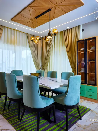 A dining space that combines bold colors and natural textures. The teal velvet chairs, marble-top table, and wood-paneled ceiling create a rich and inviting atmosphere for memorable meals.