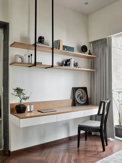 The study's entry from the living room welcomes you with a stylish herringbone-patterned wooden floor. The floating desk and suspended shelves create a sense of openness and modern sophistication.