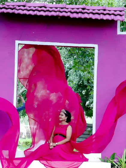 A duplicate of a creative maternity shot using a purple wall with a window cutout, with the pink fabric of the gown flowing through.