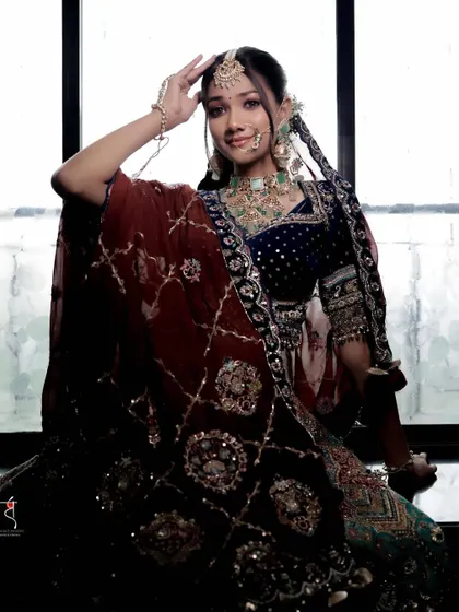 A full portrait showing a unique, multi colored lehenga paired with a deep blue velvet blouse. The makeup is kept fresh and luminous to balance the rich colors of the outfit.