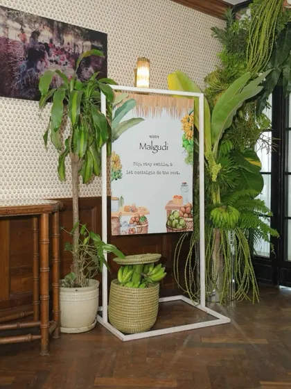 The welcome sign for the 'Malgudi' collection launch, framed by a lush arch of tropical greenery.