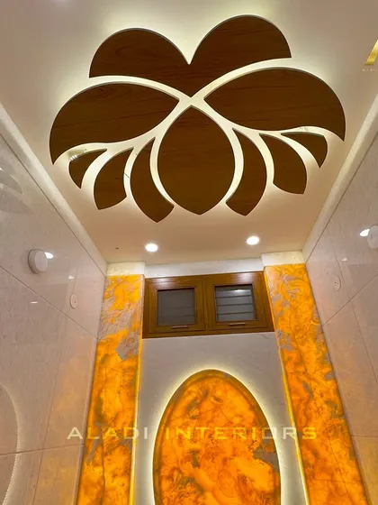 A look at the puja room's false ceiling, which features a stunning wooden lotus cutout with backlighting. The glowing onyx-style wall panels enhance the divine atmosphere.