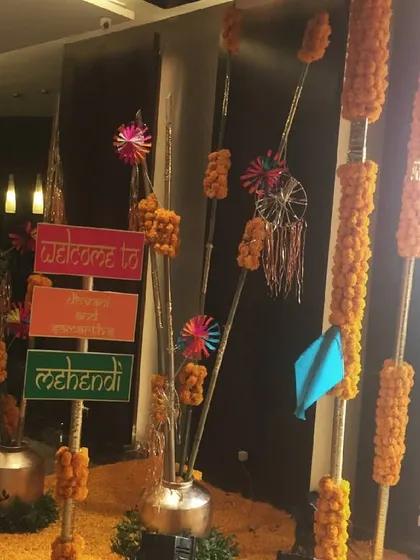 A rustic welcome corner for a Mehendi, with a colorful directional sign, marigold garlands, and whimsical paper windmills.
