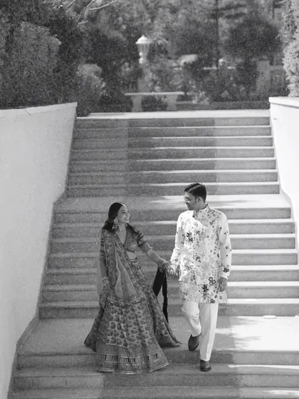 A timeless black and white shot of the couple descending a grand staircase. This classic pre-wedding photograph emphasizes the elegance of their traditional attire and the grandeur of the location.