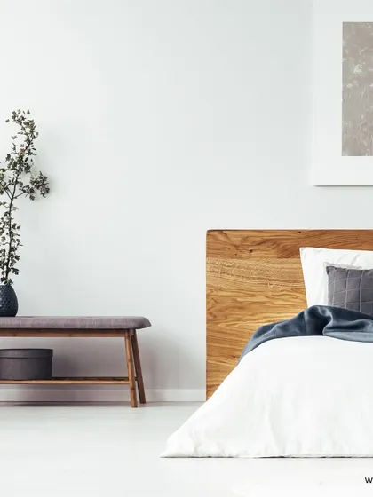 A minimalist bedroom design featuring a simple wooden headboard, a low bench, and a neutral color palette for a calm and uncluttered feel.