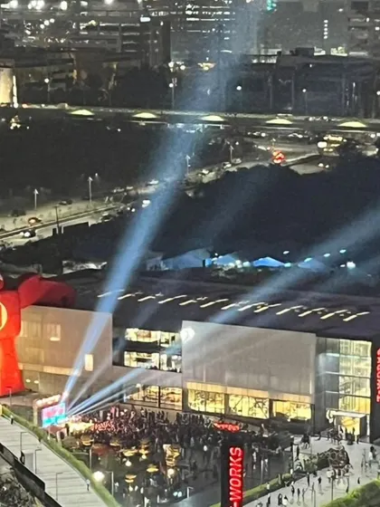 A night view of the T Works building during a community event. The simple industrial aesthetic of the building, combined with dramatic event lighting, creates an exciting atmosphere. The design prioritizes functionality and adaptability for various public uses.
