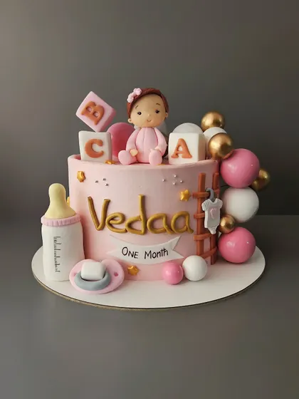 Celebrating one month in this world for baby Vedaa. This pretty pink chocolate truffle cake is adorned with baby essentials like blocks, a pacifier, and a milk bottle.