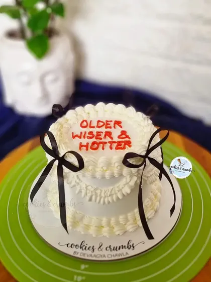 "Older, Wiser & Hotter." A fun and sassy vintage-style cake with piped ruffles and black bows, perfect for a birthday celebration with a sense of humor.