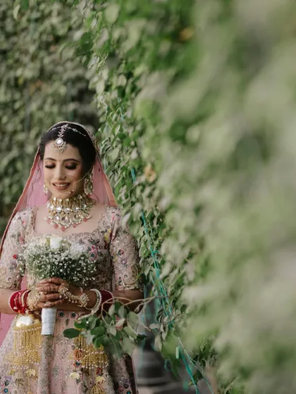 A beautiful portrait of the bride holding her bouquet, set against a lush green wall, looking serene and happy.