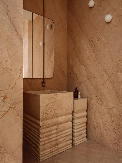 This powder room is a monolithic moment in blush-colored marble, with a sculptural, fluted pedestal sink that feels both ancient and modern.