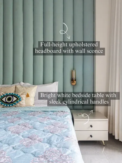 A full-height upholstered headboard in a soft mint green is paired with a bright white bedside table. The sleek cylindrical handles and brass wall sconce are small details that complete the look.