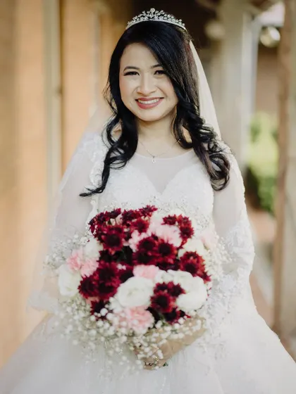 A classic portrait of a smiling Christian bride, holding her bouquet of red and white flowers. Her happiness radiates from the photo, capturing the joy of her wedding day.