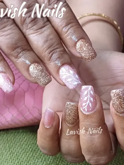 A beautiful mix of rose gold and pink glitter nails with a hand-painted white leaf design on an accent nail, perfect for a sophisticated look.