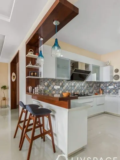 This kitchen features a stylish breakfast bar with a wooden overhang and elegant pendant lights. The patterned backsplash adds a touch of bohemian flair to the modern white cabinets.