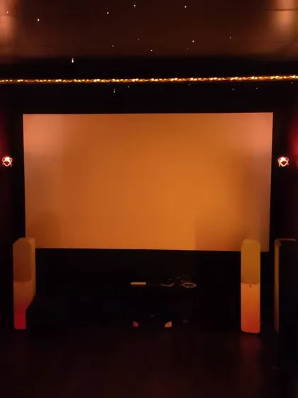 This image showcases the front of a modern theater before the movie starts. The setup includes a large projection screen, tower speakers, and subtle fairy light accents for a touch of ambiance.