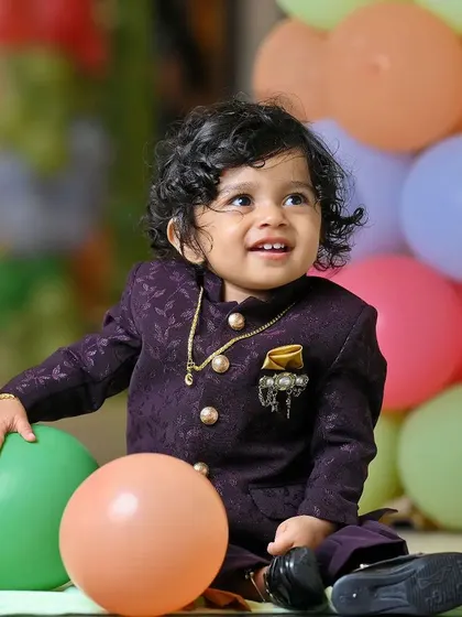 A candid portrait of a young boy with curly hair, smiling as he plays with balloons at his party. We aim to capture these natural, happy expressions that show a child's true personality.