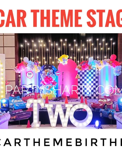 A vibrant car-themed stage for a second birthday, with 'TWO' in marquee letters and cutouts of characters from Disney's Cars.