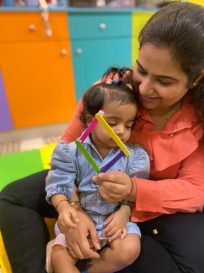 A mother looks on lovingly as her child examines the popsicle stick shape they made together.