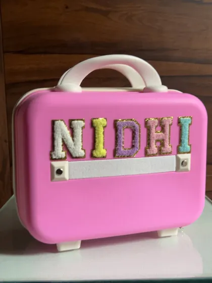 The personalized pink mini-suitcase for baby Nidhi, adorned with her name in colorful, fuzzy letters.
