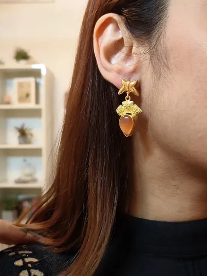 A close-up of the formal embellished drop earrings with an orange stone, perfect for adding a subtle pop of colour.