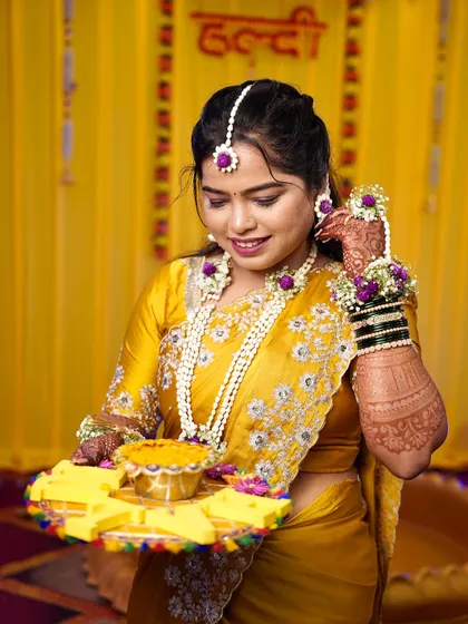 A candid moment of the Haldi bride. The hairstyle is simple yet elegant, allowing the vibrant colors of her outfit and the floral jewelry to stand out.