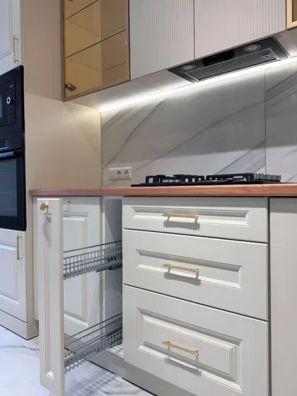 This view highlights the practical storage solutions within our classic kitchen designs, such as this pull-out wire basket drawer, perfect for organizing bottles and jars.