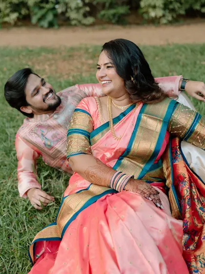 A joyful, candid moment of a couple in beautiful traditional Indian attire, laughing together while relaxing on the grass in a park. This highlights my ability to capture unposed, natural laughter during an engagement photoshoot.